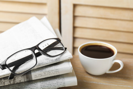 Stack of newspapers, coffee and glasses on wooden table, closeupの写真素材