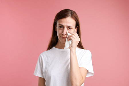 Woman crying and wiping tears on pink backgroundの写真素材