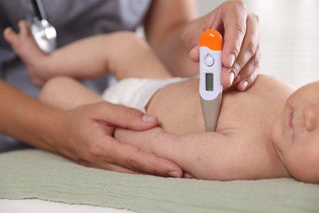 Pediatrician examining little child with thermometer in hospital, closeup. Checking baby's healthの写真素材