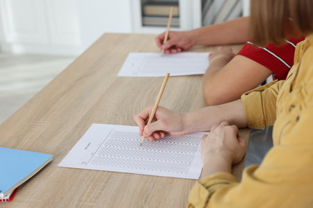 Students taking exam at wooden table indoors, closeupの写真素材