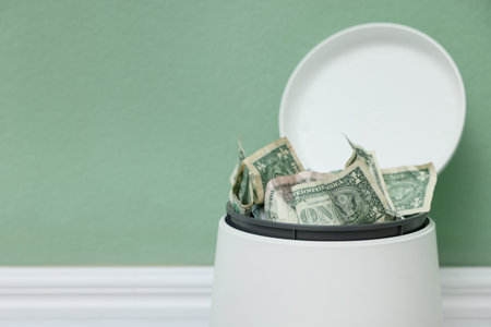 Dollar banknotes in trash bin near green wall indoors, closeup. Space for textの写真素材