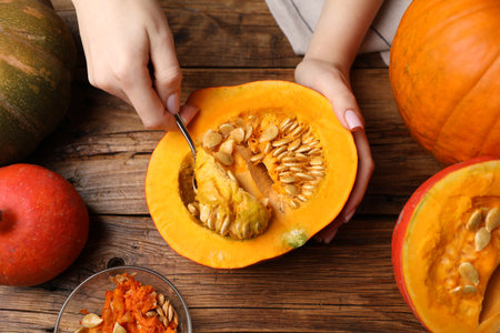Woman removing seeds from raw pumpkin at wooden table, top viewの写真素材