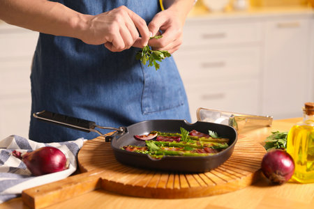 Man adding parsley into pan with grilled vegetables at table indoors, closeupの写真素材