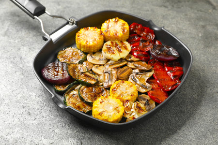 Delicious grilled vegetables and mushrooms in pan on gray textured table, closeupの写真素材