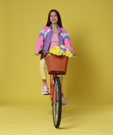 Smiling woman riding bicycle with basket of flowers on green backgroundの写真素材