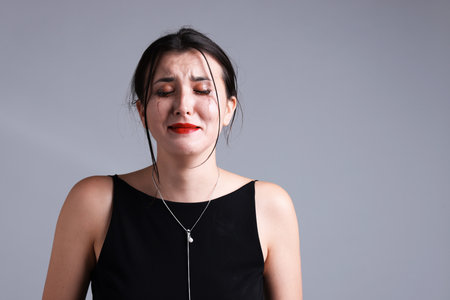 Woman with smeared mascara in dress crying on gray background. Space for textの写真素材