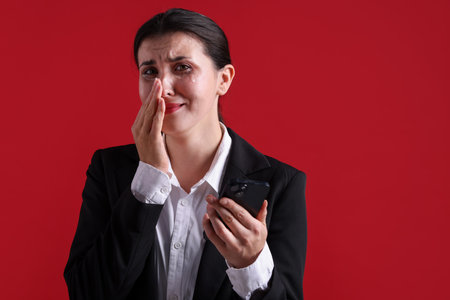 Businesswoman in suit with smartphone crying on red background.の写真素材