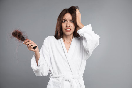 Woman with brush and lost hair on gray background. Alopecia problemの写真素材