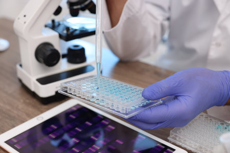 Research in genetics. Scientist with micropipette and microplate working at table in laboratory, closeupの写真素材