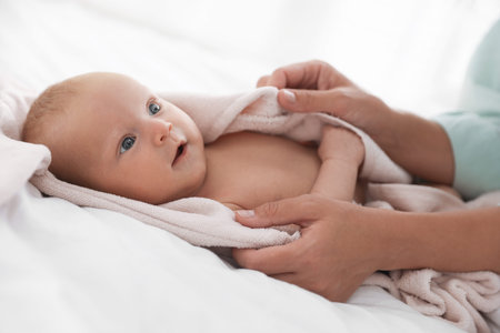 Mother covering her baby with towel after bathing on bed, closeup