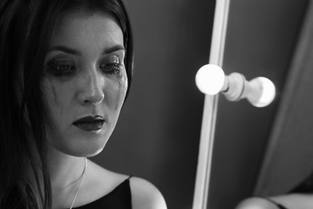 Woman with smeared mascara crying near mirror indoors, space for text. Black and white effectの写真素材