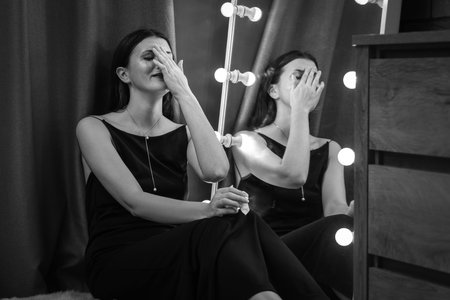 Woman crying near mirror indoors. Black and white effectの写真素材