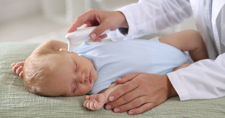 Pediatrician examining little child with infrared thermometer in hospital, closeup. Checking baby's healthの写真素材