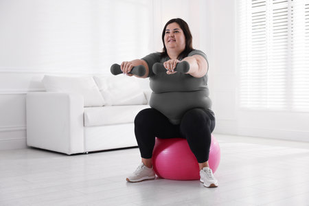 Smiling woman in sportswear training with dumbbells and fitness ball at home. Space for textの写真素材
