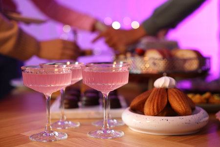 Glasses of cocktails and people with delicious desserts at buffet table, selective focusの写真素材