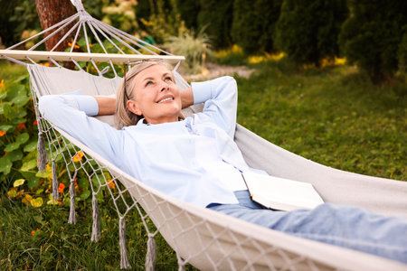 Senior woman with book resting in hammock outdoorsの写真素材
