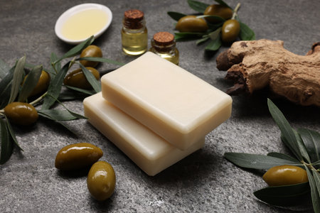 Handmade soap bars, olives, green leaves and oil on gray textured background, closeupの写真素材