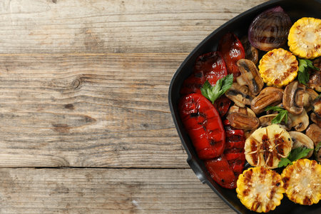 Delicious grilled vegetables, mushrooms and parsley in pan on wooden table, top view. Space for textの写真素材