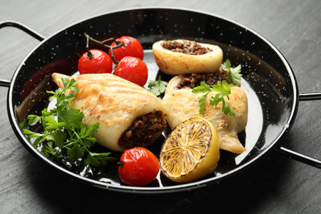 Pieces of tasty grilled squid stuffed with mushrooms, parsley, tomatoes and lemon in pan on dark...