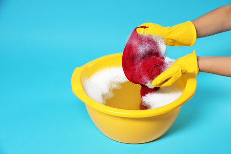 Woman washing clothes in plastic basin on light blue background, closeup. Space for textの写真素材