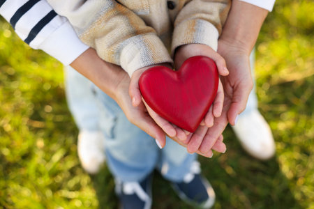 Mother with her son holding red wooden heart together outdoors, above view. Family bondingの写真素材