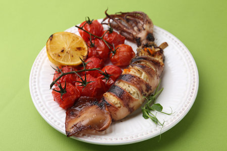 Tasty stuffed squid, microgreens, lemon and tomatoes on green background, closeup