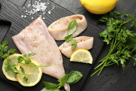 Pieces of raw squid, lemon and herbs on black table, flat layの写真素材