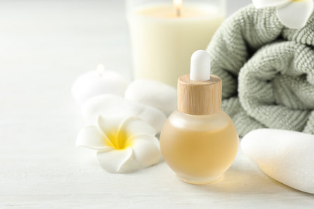 Essential oil, towel, burning candles, plumeria flower and spa stones on white table, closeup. Space for textの写真素材