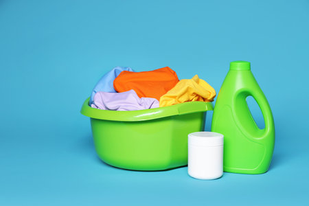 Plastic basin with laundry and detergents on light blue backgroundの写真素材