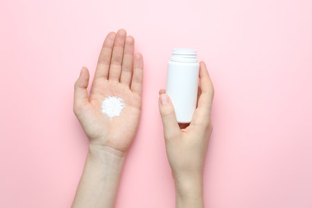 Woman with bottle of talcum powder on pink background, top viewの写真素材