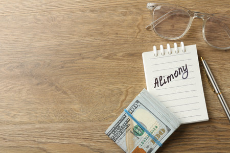 Notebook with word Alimony, money, pen and glasses on wooden table, flat lay. Space for textの写真素材
