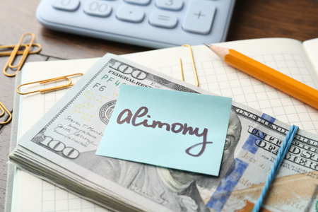 Note with word Alimony, money, notebook, pencil, clips and calculator on wooden table, closeupの写真素材