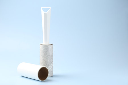 Lint roller with used sticky tape and new adhesive roll on light blue background, space for textの写真素材