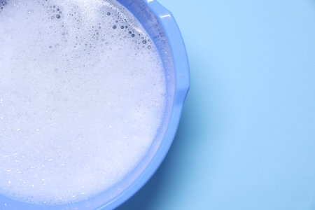 Plastic basin with water and foam on light blue background, top view. Space for textの写真素材