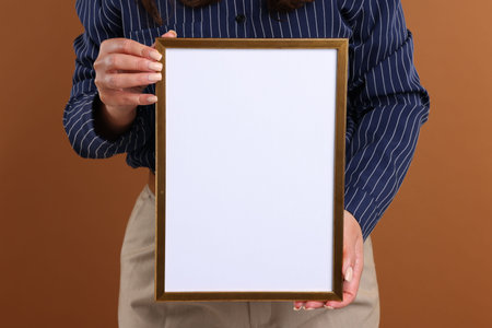 Woman with blank frame on brown background, closeup. Mockup for designの写真素材