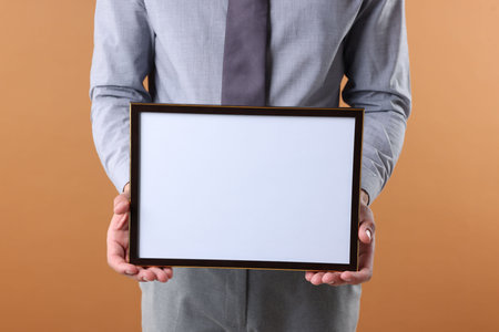 Man with diploma blank frame on pale orange background, closeup. Mockup for designの写真素材