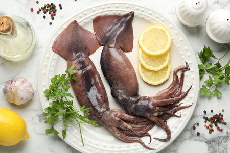 Raw squids, lemon and other products on white marble table, flat lay