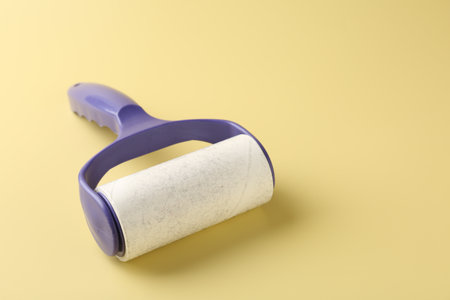 Lint roller with used sticky tape on yellow background, closeup. Space for textの写真素材