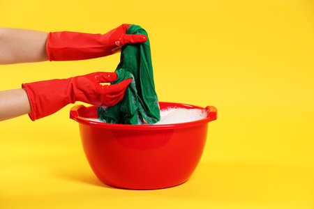 Woman washing clothes in plastic basin on yellow background, closeupの写真素材