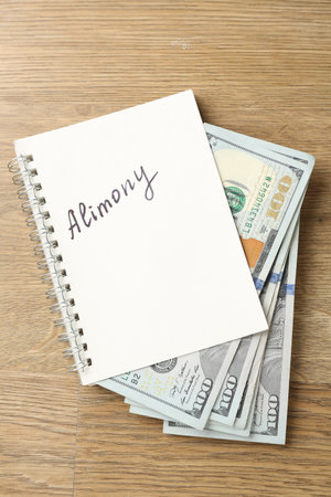 Notebook with word alimony and money on wooden table, top viewの写真素材