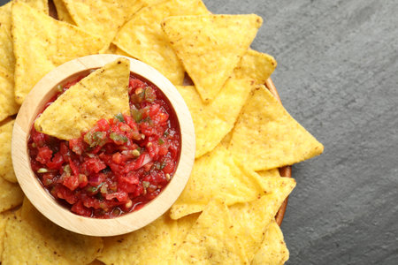 Tasty salsa in bowl and nachos on black table, top view. Space for text
