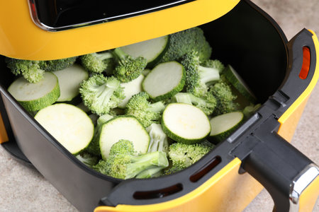 Raw broccoli and cut zucchini in air fryer on gray table, closeupの写真素材