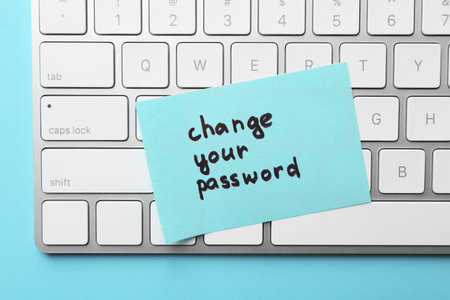 Note with phrase Change your password and keyboard on light blue background, top view
