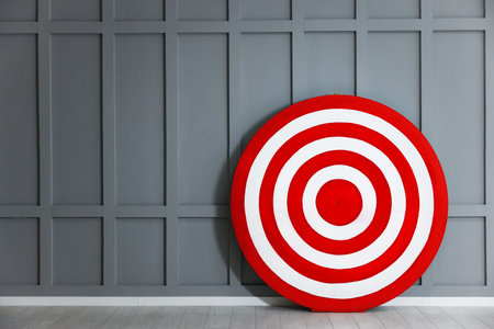 Round shooting target on floor near gray wall, space for text