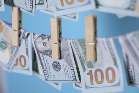 Money laundering. Banknotes hanging on clothesline against light blue background, closeup