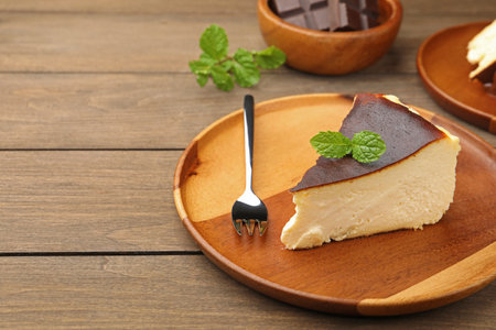 Piece of delicious Basque cheesecake with mint and chocolate on wooden table, closeup. Space for textの写真素材