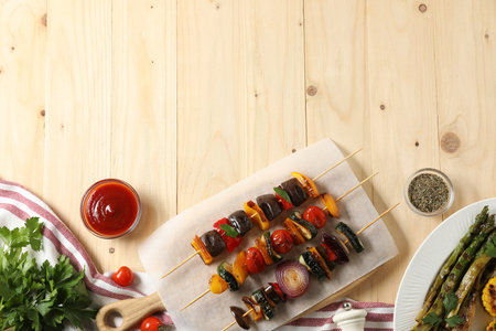Skewers with tasty grilled vegetables served on wooden table, flat lay. Space for textの写真素材