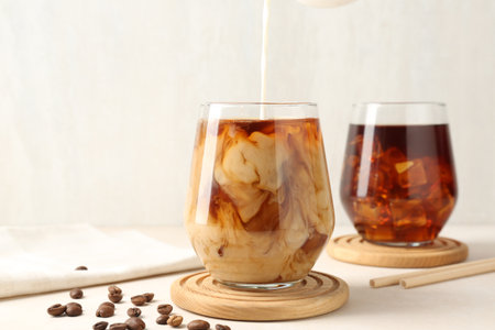 Pouring milk into glass of iced coffee at white table, closeupの写真素材