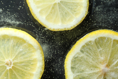 Slices of lemon in soda water on dark background, flat layの写真素材
