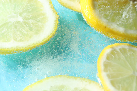 Slices of lemon in soda water on light blue background, closeup